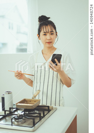 A woman cooking in the kitchen while checking a recipe on her smartphone. A woman cooking in the kitchen while checking a recipe on her smartphone. 140948724