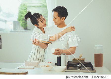 A smiling couple, with the man leaning against her while she cooks in the kitchen. A smiling couple, with the man leaning against her while she cooks in the kitchen. 140948818