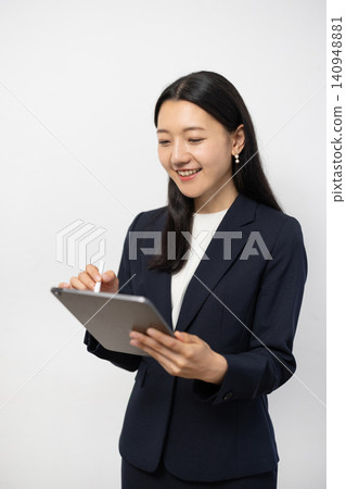 A young Japanese businesswoman operates a tablet in front of a white wall. A young Japanese businesswoman operates a tablet in front of a white wall. 140948881