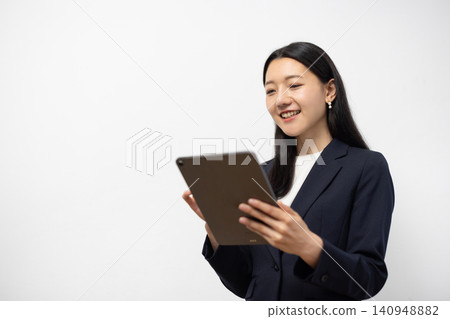 A young Japanese businesswoman operates a tablet in front of a white wall. A young Japanese businesswoman operates a tablet in front of a white wall. 140948882