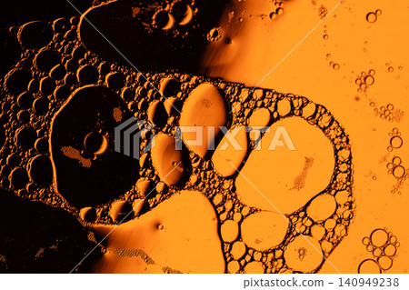 Macro view of suspended oil droplets and tiny bubbles forming organic shapes against warm orange light with dark contrast and fluid texture Macro view of suspended oil droplets and tiny bubbles forming organic shapes against warm orange light with dark contrast and fluid texture 140949238