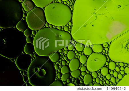 Close macro view shows translucent green oil droplets suspended in liquid, forming organic circular patterns, glossy surfaces, and dramatic dark background Close macro view shows translucent green oil droplets suspended in liquid, forming organic circular patterns, glossy surfaces, and dramatic dark background 140949242
