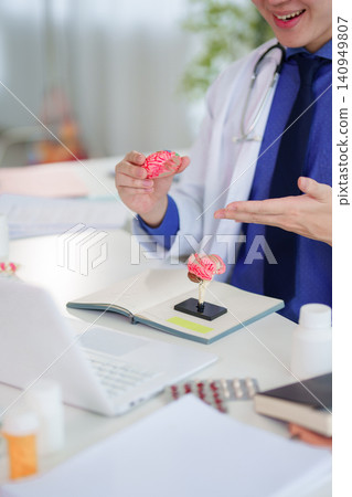 Smiling Asian doctor presenting brain anatomy model to patient during neurology consultation in modern clinic Smiling Asian doctor presenting brain anatomy model to patient during neurology consultation in modern clinic 140949807