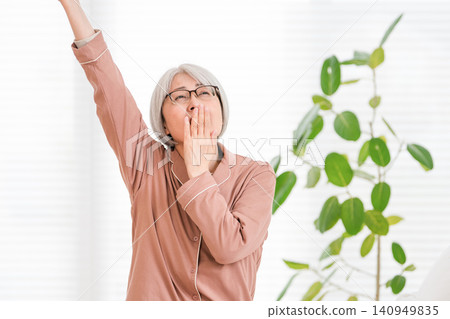 A senior woman in her pajamas stretches after waking up. A senior woman in her pajamas stretches after waking up. 140949835
