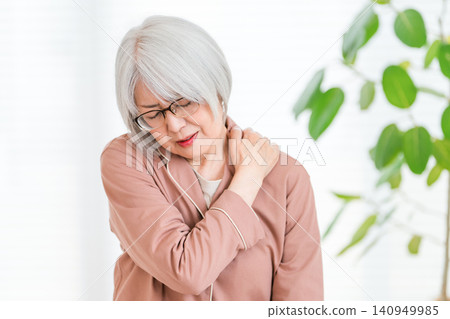 A senior woman with gray hair in her pajamas, suffering from stiff shoulders. A senior woman with gray hair in her pajamas, suffering from stiff shoulders. 140949985