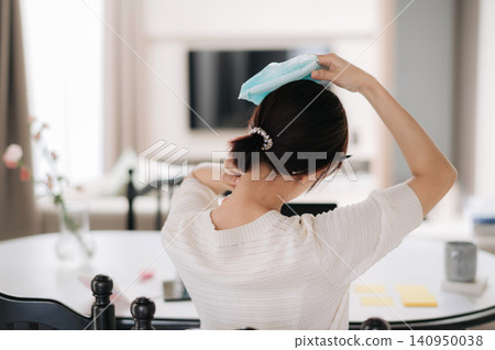 Asian woman cold compress headache pain relief home scene with back view of adult female holding cool cloth on head in bright room for migraine care and wellness Asian woman cold compress headache pain relief home scene with back view of adult female holding cool cloth on head in bright room for migraine care and wellness 140950038