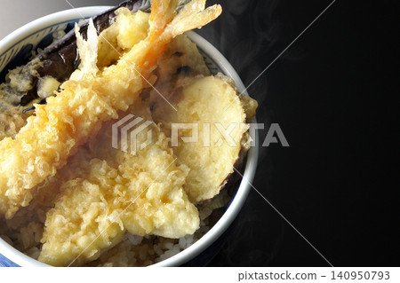 A single serving of piping hot tempura rice bowl photographed against a black background. A single serving of piping hot tempura rice bowl photographed against a black background. 140950793