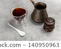 Cup of coffee, a cezve and chocolate-dipped cookies on the kitchen table. 140950963