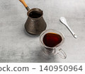 Cup of coffee, a cezve and a spoon on the kitchen table. 140950964