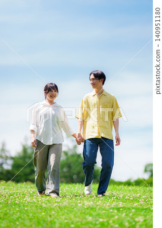 A couple walking in a park under a blue sky A couple walking in a park under a blue sky 140951180