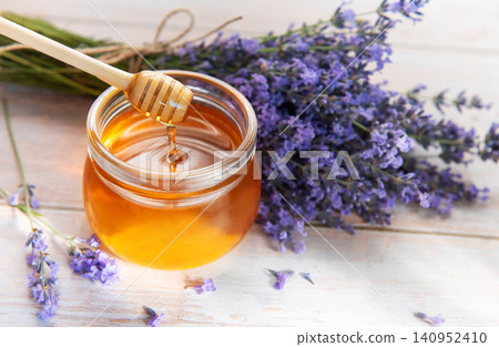 Honey dripping from dipper into jar with lavender flowers Honey dripping from dipper into jar with lavender flowers 140952410