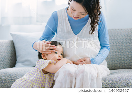 一個小女孩依偎在她懷孕的母親身邊，兩人在客廳玩耍。 140952467