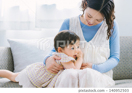 一個小女孩依偎在她懷孕的母親身邊，兩人在客廳玩耍。 140952503