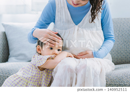 一個小女孩依偎在她懷孕的母親身邊,兩人在客廳玩耍。 一個小女孩依偎在她懷孕的母親身邊,兩人在客廳玩耍。 140952511