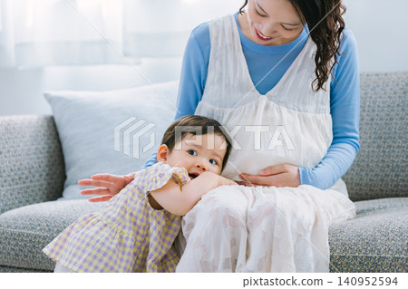 A little girl cuddling with her pregnant mother in the living room. A little girl cuddling with her pregnant mother in the living room. 140952594