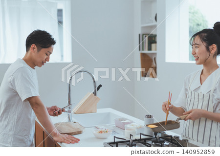 廚房場景,一名男子正在用智慧型手機查看食譜,旁邊有一位微笑的女子。 廚房場景,一名男子正在用智慧型手機查看食譜,旁邊有一位微笑的女子。 140952859