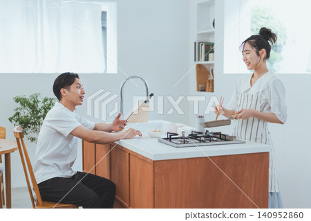 廚房場景,一名男子坐在椅子上,一邊和正在煮飯的女友聊天。 廚房場景,一名男子坐在椅子上,一邊和正在煮飯的女友聊天。 140952860