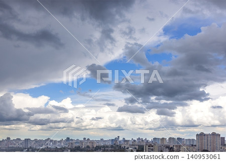 Cloudy sky over city buildings with blue patches and gray clouds in afternoon light Cloudy sky over city buildings with blue patches and gray clouds in afternoon light 140953061