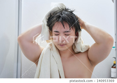 一名二十多歲的男子正在用浴巾擦頭。 一名二十多歲的男子正在用浴巾擦頭。 140953369