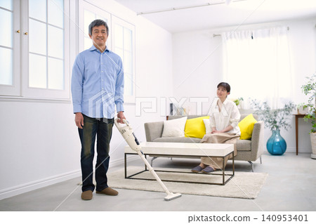 一位微笑的男士和一位六十多歲的女士一邊聊天一邊使用吸塵器。 一位微笑的男士和一位六十多歲的女士一邊聊天一邊使用吸塵器。 140953401
