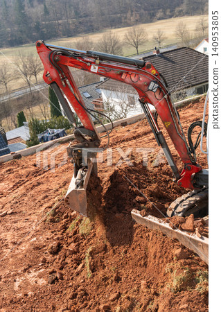 The excavators bucket is loaded with clay and stones as it digs into the earth. The powerful machine is at work on the construction site, preparing the ground for the next phase of the project. The excavators bucket is loaded with clay and stones as it digs into the earth. The powerful machine is at work on the construction site, preparing the ground for the next phase of the project. 140953805