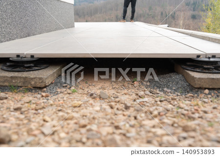 A close-up of an adjustable pedestal system supporting raised outdoor tiles. This innovative method ensures stability, proper drainage, and a level surface, making it ideal for terraces and patios A close-up of an adjustable pedestal system supporting raised outdoor tiles. This innovative method ensures stability, proper drainage, and a level surface, making it ideal for terraces and patios 140953893