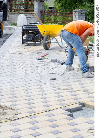 Worker lays bricks on a new path using a power tool at a residential area in bright daytime Worker lays bricks on a new path using a power tool at a residential area in bright daytime 140953907