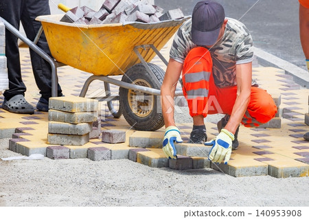 Workers lay down bricks for pavement on a city street during daylight hours in an urban area Workers lay down bricks for pavement on a city street during daylight hours in an urban area 140953908