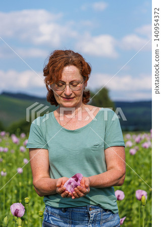 Woman standing in a blooming pink poppy field and holding delicate poppy petals in her hands. Woman standing in a blooming pink poppy field and holding delicate poppy petals in her hands. 140954372