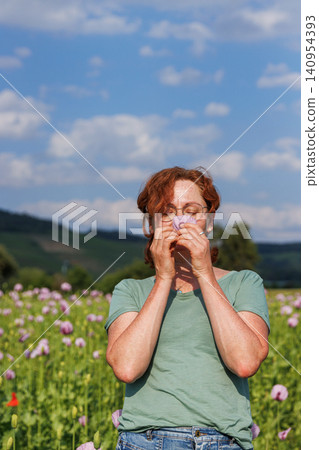 Mature woman smelling pink poppy petals in blooming summer field Mature woman smelling pink poppy petals in blooming summer field 140954393