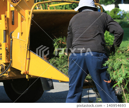 Worker Loads Branches Into a Yellow Wood Chipper Worker Loads Branches Into a Yellow Wood Chipper 140954693