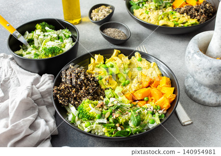 A quinoa bowl is arranged with roasted pumpkin, hummus, and a fresh salad. Plates are set on a table with utensils. Sunshine comes through the window A quinoa bowl is arranged with roasted pumpkin, hummus, and a fresh salad. Plates are set on a table with utensils. Sunshine comes through the window 140954981