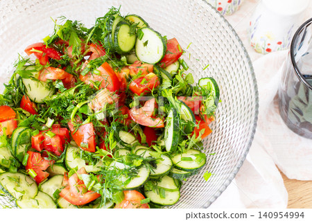 A bowl filled with a salad of sliced tomatoes and cucumbers mixed with onions, dill, and parsley is ready to be served. Ingredients are fresh from local farms A bowl filled with a salad of sliced tomatoes and cucumbers mixed with onions, dill, and parsley is ready to be served. Ingredients are fresh from local farms 140954994