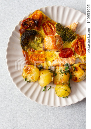 Baked potatoes are served with salmon, broccoli, and tomatoes on a plate. This meal is a good option for breakfast or lunch, offering a balance of nutrition and taste 140955005