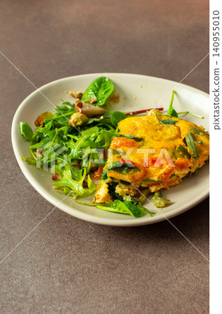 A plate holds baked vegetables combined with eggs alongside a salad of arugula and Brussels sprouts. This meal is perfect for breakfast or lunch, providing healthy nutrients A plate holds baked vegetables combined with eggs alongside a salad of arugula and Brussels sprouts. This meal is perfect for breakfast or lunch, providing healthy nutrients 140955010