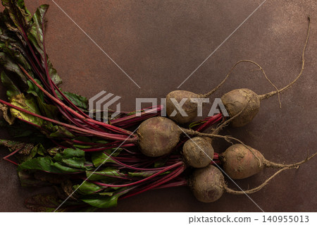 Beets with green leaves rest on a brown surface in a kitchen. The setting is warm and hints at fresh produce ready for cooking or eating Beets with green leaves rest on a brown surface in a kitchen. The setting is warm and hints at fresh produce ready for cooking or eating 140955013