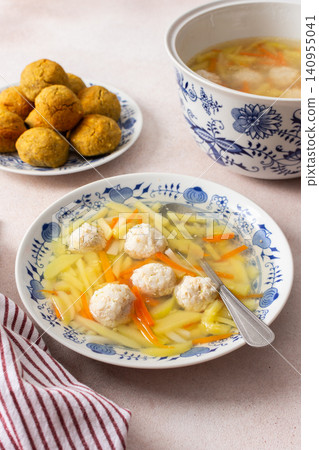 A bowl of vegetable soup with chicken meatballs is served alongside chickpea buns on a table. Fresh ingredients create a hearty meal for breakfast or lunch A bowl of vegetable soup with chicken meatballs is served alongside chickpea buns on a table. Fresh ingredients create a hearty meal for breakfast or lunch 140955041