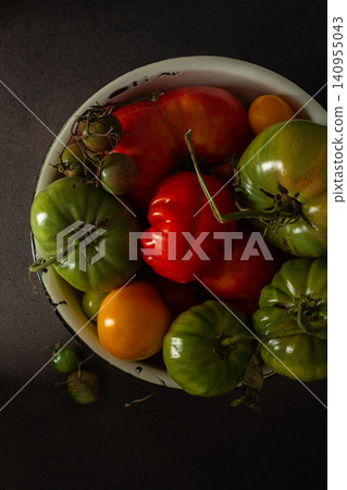 A bowl holds different types of tomatoes and peppers in various colors and sizes. The setting is simple with a dark background and natural lighting A bowl holds different types of tomatoes and peppers in various colors and sizes. The setting is simple with a dark background and natural lighting 140955043