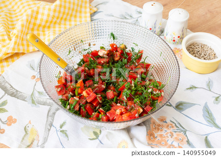 A bowl holds a salad made from diced tomatoes, onions, and dill, topped with sunflower seeds. The setting shows a warm summer day with kitchen items around A bowl holds a salad made from diced tomatoes, onions, and dill, topped with sunflower seeds. The setting shows a warm summer day with kitchen items around 140955049