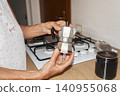 Holding Stovetop Moka Pot Beside Ground Coffee Container 140955068