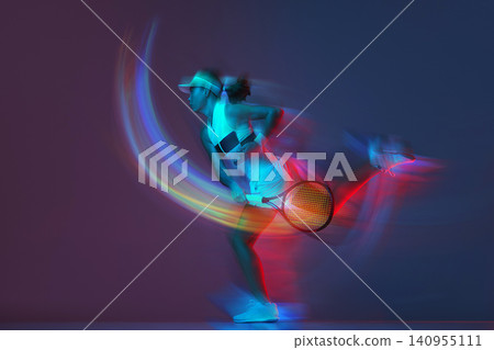 Female tennis player serving with colorful light trails in dynamic studio portrait. 140955111