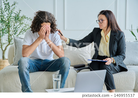 Psychologist comforting crying teen boy in office Psychologist comforting crying teen boy in office 140955537