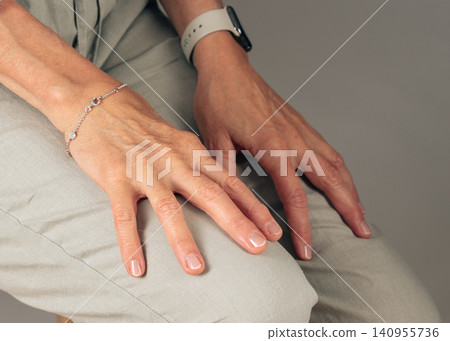 A close-up top-down view of hands resting on fabric, adorned with a bracelet and smartwatch, set against a neutral indoor background. The scene is casual and relaxed, featuring gray and off. A close-up top-down view of hands resting on fabric, adorned with a bracelet and smartwatch, set against a neutral indoor background. The scene is casual and relaxed, featuring gray and off. 140955736