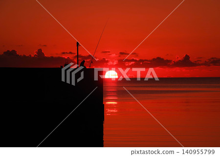 宮古島漁港的日出,沐浴在鮮豔的紅光中,漁民們站在防波堤上的身影清晰可見。 宮古島漁港的日出,沐浴在鮮豔的紅光中,漁民們站在防波堤上的身影清晰可見。 140955799
