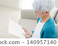 一位老婦人坐在沙發上看書。 140957140