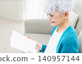 一位老婦人坐在沙發上看書。 140957144