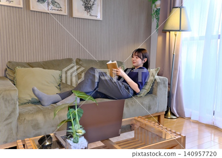 A relaxing "me time." A peaceful lifestyle scene of a woman engrossed in reading while lying on the sofa. A relaxing "me time." A peaceful lifestyle scene of a woman engrossed in reading while lying on the sofa. 140957720