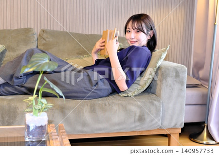 A relaxing "me time." A peaceful lifestyle scene of a woman engrossed in reading while lying on the sofa. A relaxing "me time." A peaceful lifestyle scene of a woman engrossed in reading while lying on the sofa. 140957733