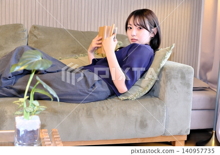 A relaxing "me time." A peaceful lifestyle scene of a woman engrossed in reading while lying on the sofa. 140957735