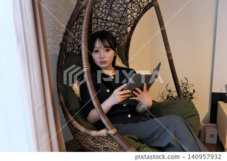 A woman relaxing in a hanging chair in the living room. 140957932